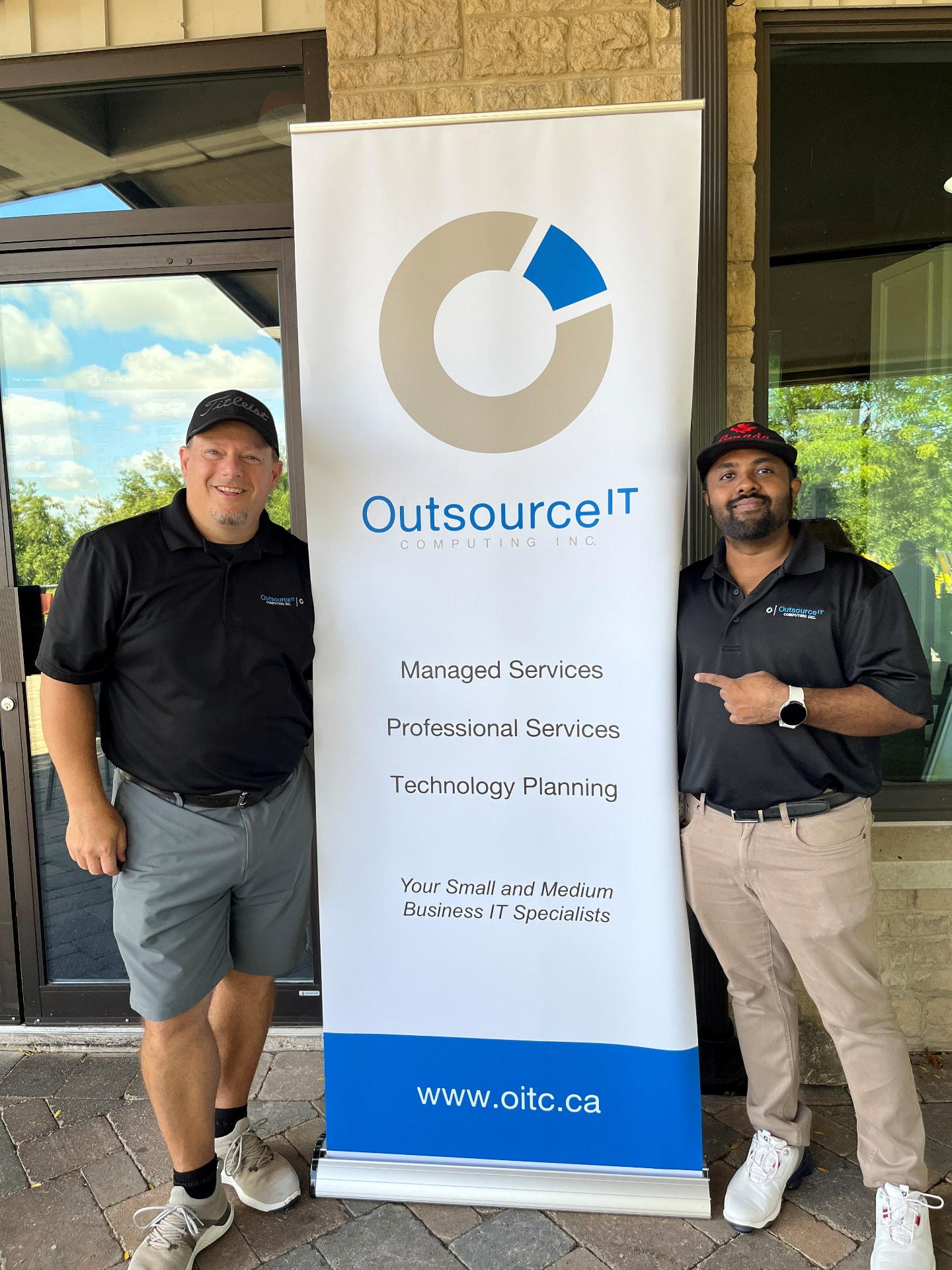 Two members of the Outsource IT team beside the Outsource IT Computing banner at the Bethany Lodge Golf Tournament
